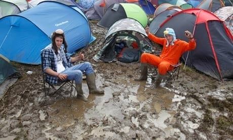 Campister sidder foran farverige telte på en våd, mudret campingplads